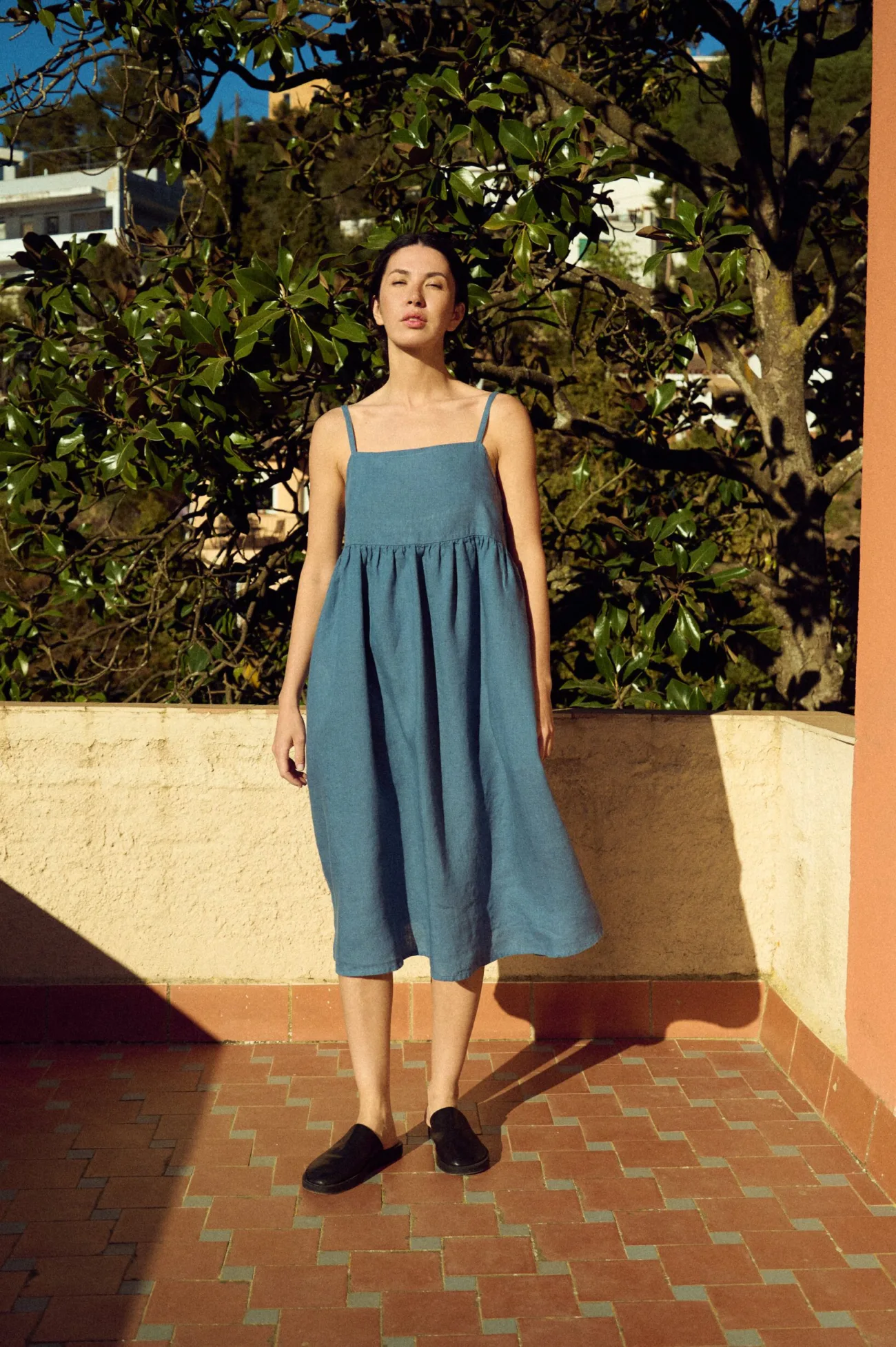 woman wearing blue linen summer midi dress with spaghetti straps, pockets and gathered skirt