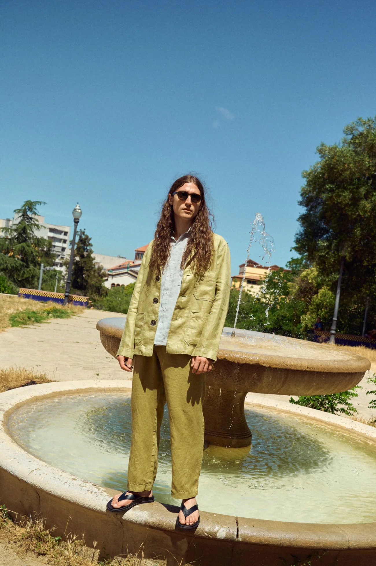 Men’s olive heavy linen jacket with an easy, slightly oversized cut, finished with notched lapels, dark buttons and spacious front pockets, paired with an ice grey linen shirt and olive linen trousers