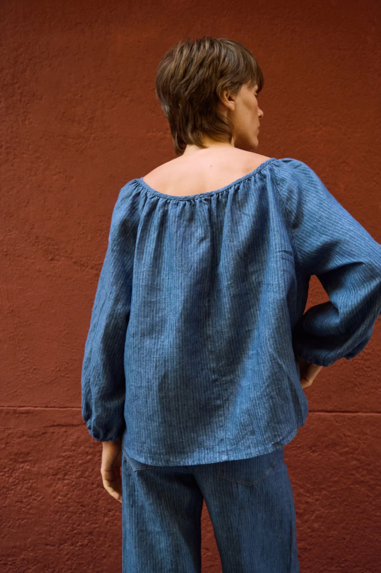 Rear view of a blue striped linen blouse with a gathered neckline and voluminous long sleeves