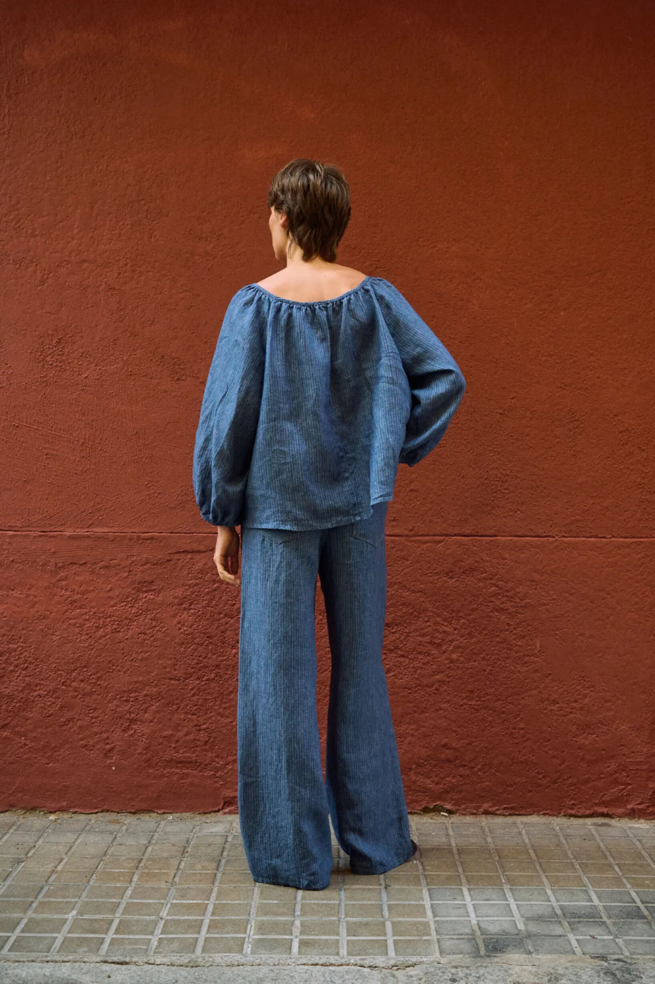 Back view of a blue striped linen blouse with a gathered neckline and voluminous sleeves, paired with matching wide-leg pants