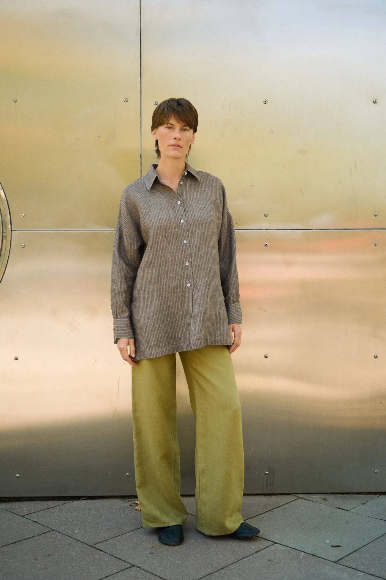 Olive heavy linen wide-leg trousers with a relaxed full-length fit, styled with an oversized brown striped linen shirt
