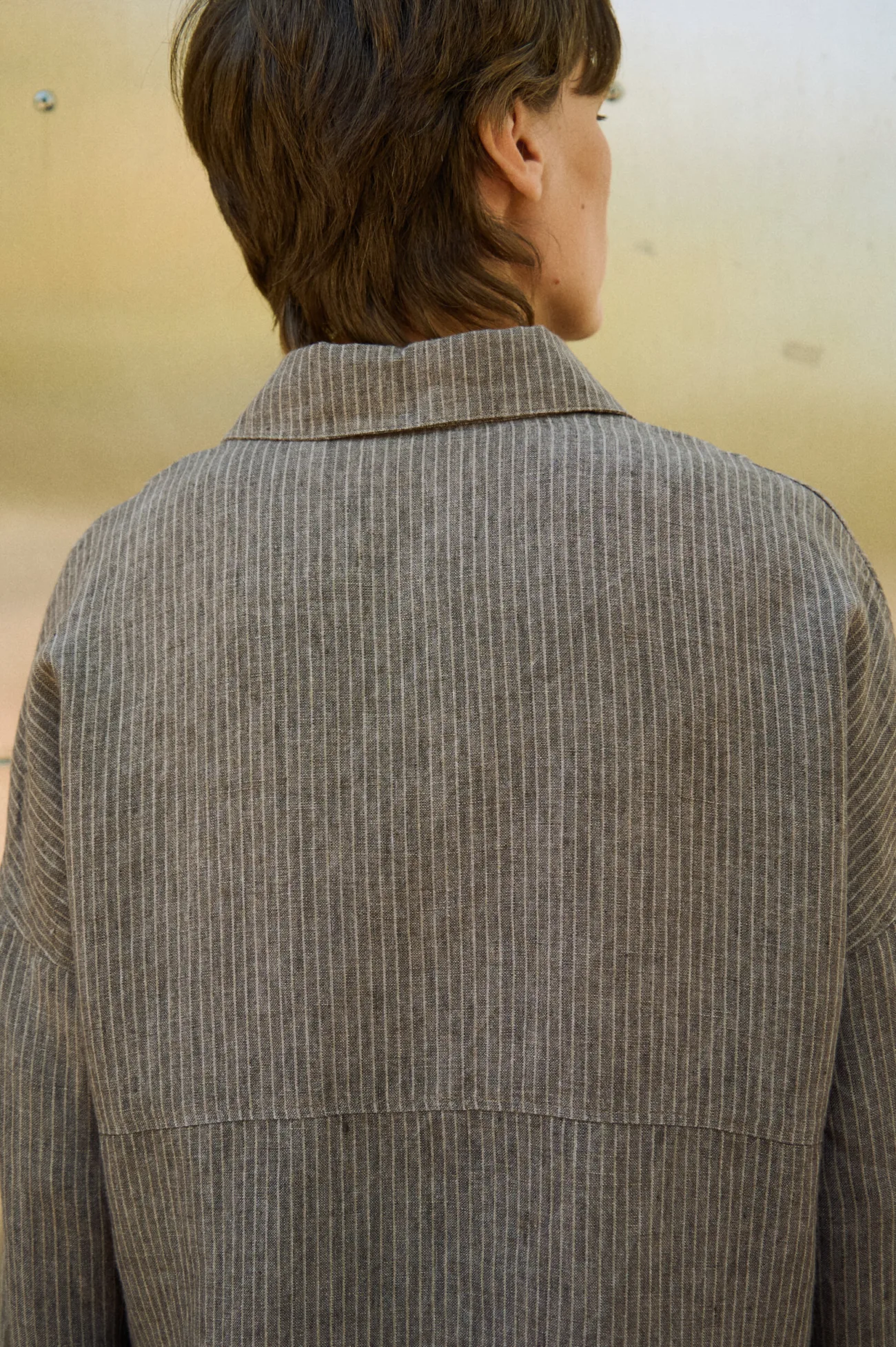 Close-up back view of a brown striped linen shirt showing the pointed collar, dropped shoulders and horizontal back seam