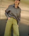 Close-up of olive heavy linen pants showing the front button closure and curved side pocket, styled with a brown striped linen shirt