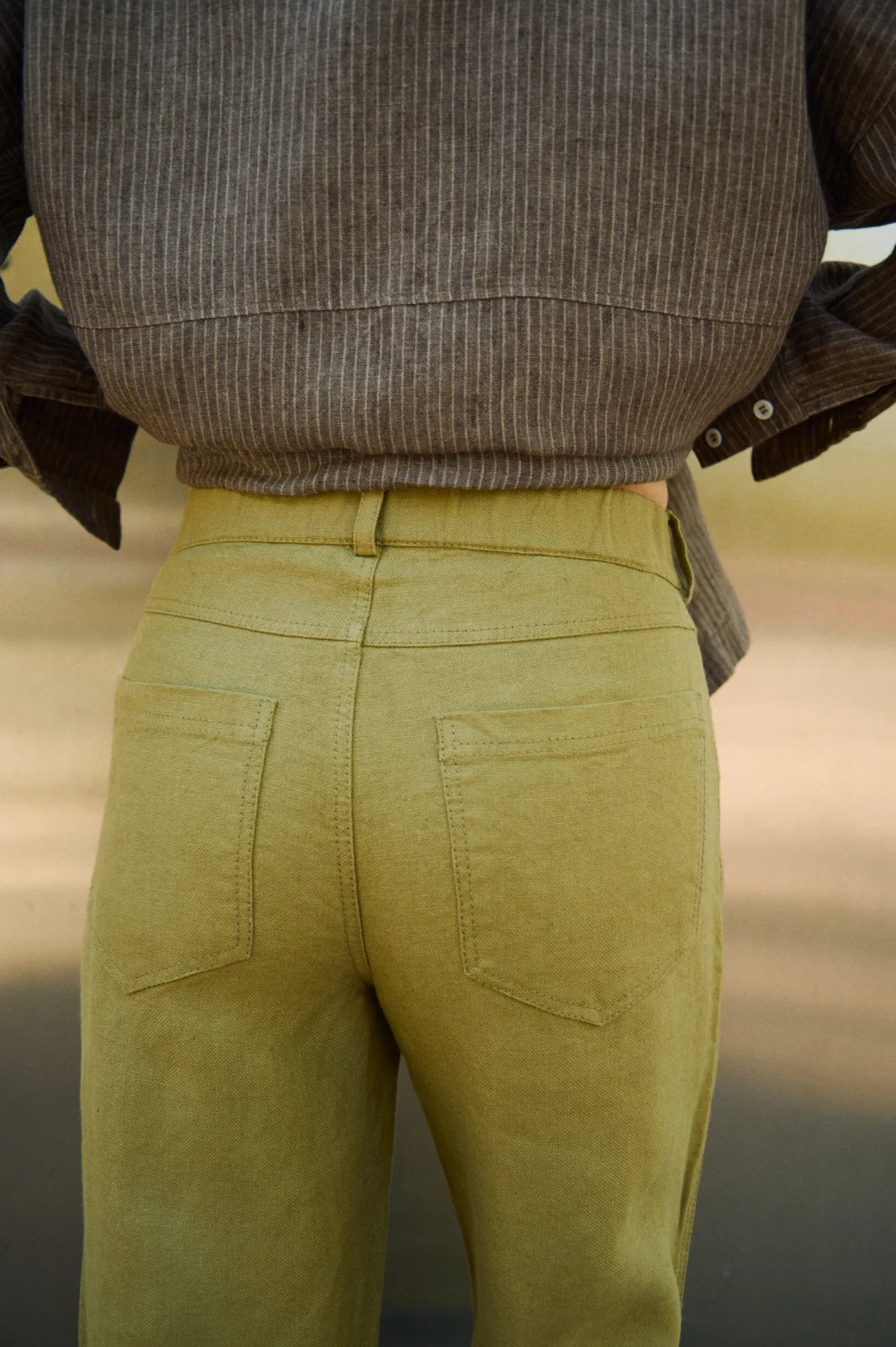 Close-up back view of olive heavy linen trousers showing the waistband, belt loops and patch pockets