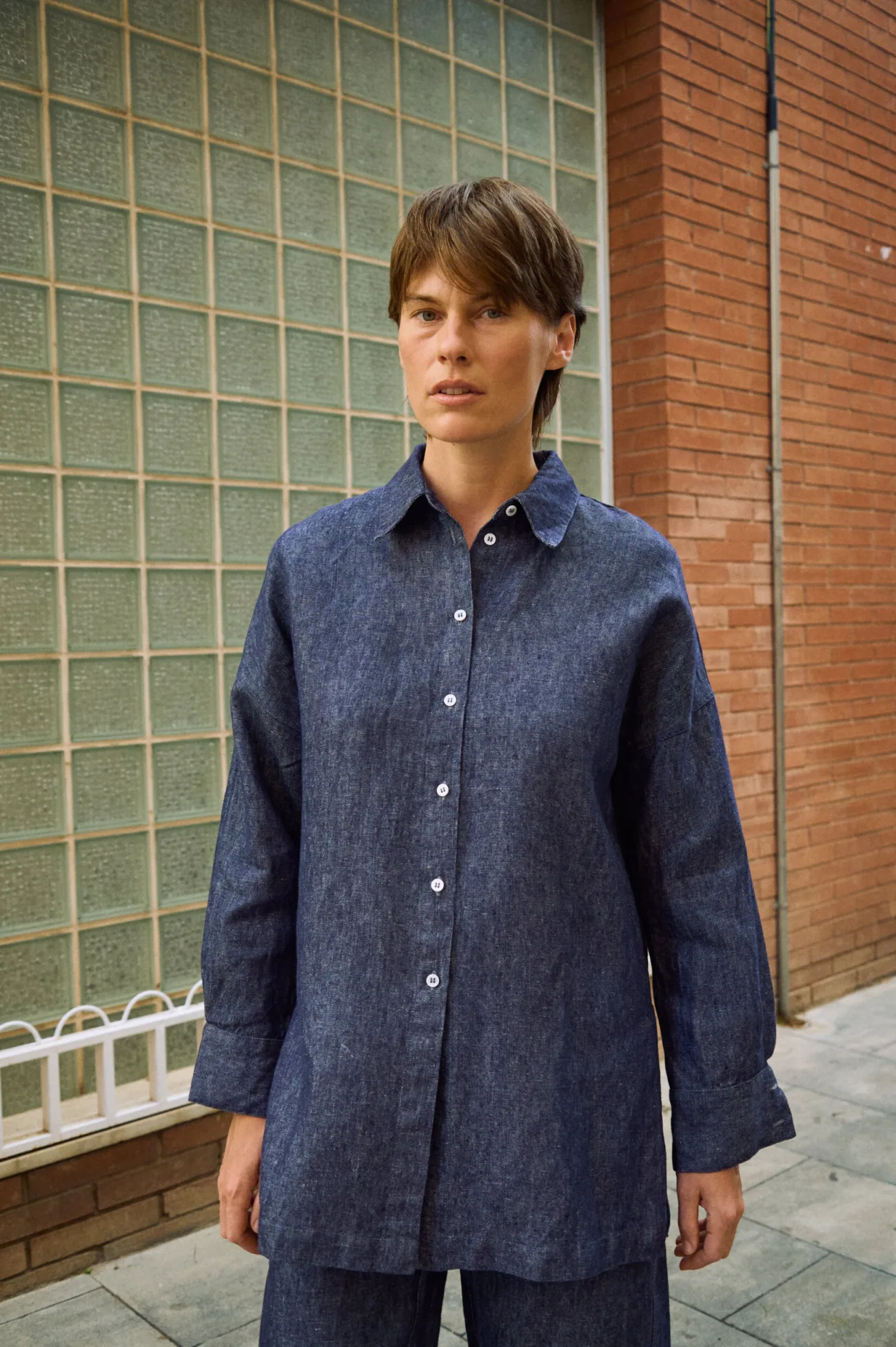 Front detail of blue denim linen shirt with button-down front, pointed collar, dropped shoulders, and wide cuffs